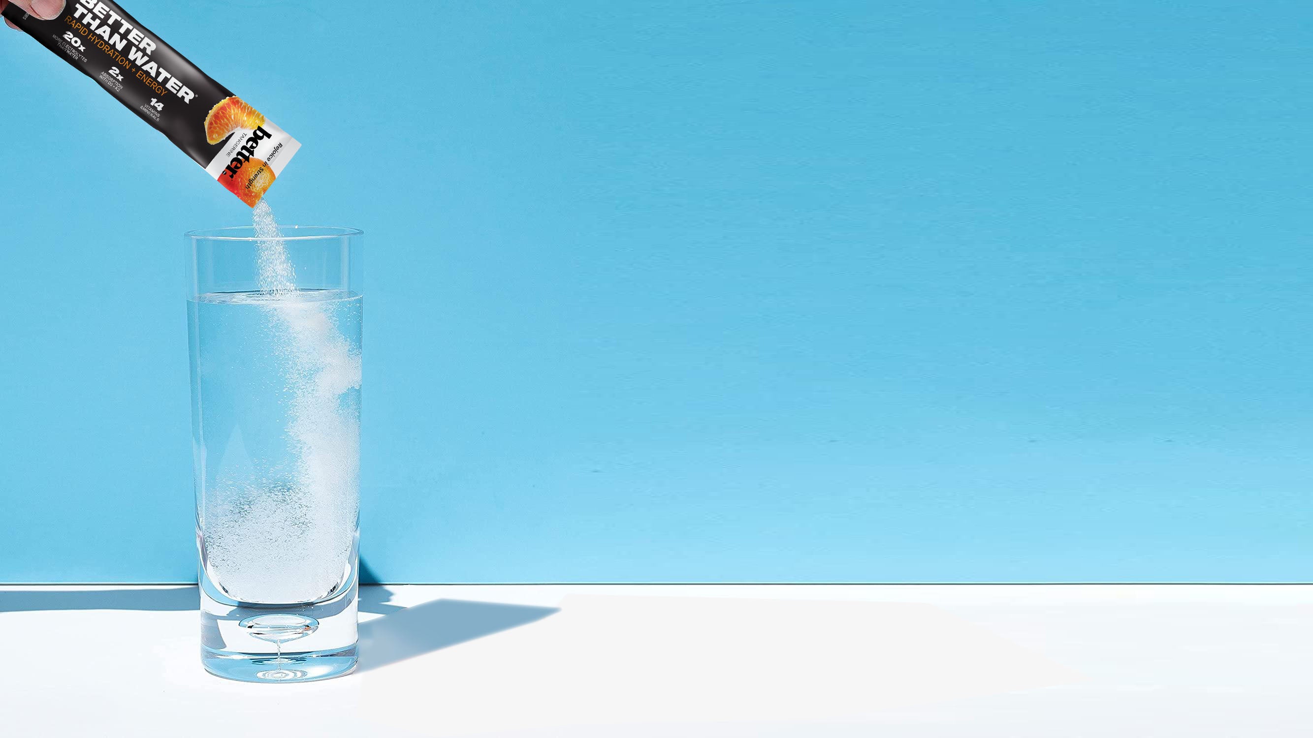 Packet of BETER hydration power being poured into a glass against a blue background